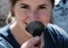 Community volunteer Katelyn Sikes holds up a flake from a groudstone adze dating to roughly 3400 years ago from the Mitks'qaaq Angayuk Site on Kodiak Island, Alaska