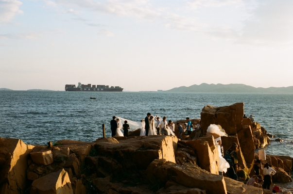 Soon-to-be-married couples crowd onto a popular outcropping in near Qingdao's historic city center for wedding portraits as a French container ship arrives to port. Photo by Hope St. John, September 2018.