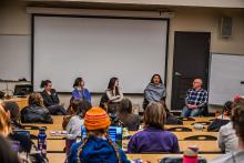 Five archaeology professionals sit at the front of a class facing students