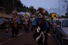 Photo of people marching in the streets at dusk, wearing black frocks painted with bones and water.