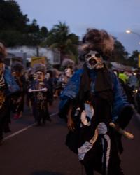 Photography of the Mas Andivagasyon carnival march by the group Klé La, Pointe-à-Pitre, Guadeloupe, February 28, 2017. Credit: Manu Louisor Photo of people marching in the streets at dusk, wearing black frocks painted with bones and water.