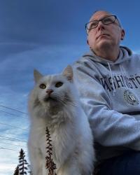 Photo of fluffy white cat and balding man with glasses wearing University of Washington sweatshirt (man is wearing sweatshirt not the cat)  taken from below making both appear gigantic.
