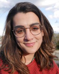 Brown-haired, brown-eyed white woman with red sweater stands before a blue Seattle sky.