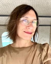 headshot of woman with brown bobbed hair and wire frame glasses in the back of a tuk tuk taxi