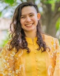 Paulina smiles wearing a yellow button-down shirt with a flower pattern on both sleeves