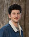 A person stands in front of a tree facing the camera wearing a jean jacket with wool insulation around the collar