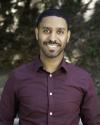 Headshot photo of male. Blurred foilage in background.