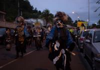 Photo of people marching in the streets at dusk, wearing black frocks painted with bones and water.