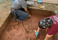 Two people excavating a shallow section at an archaeological site. 